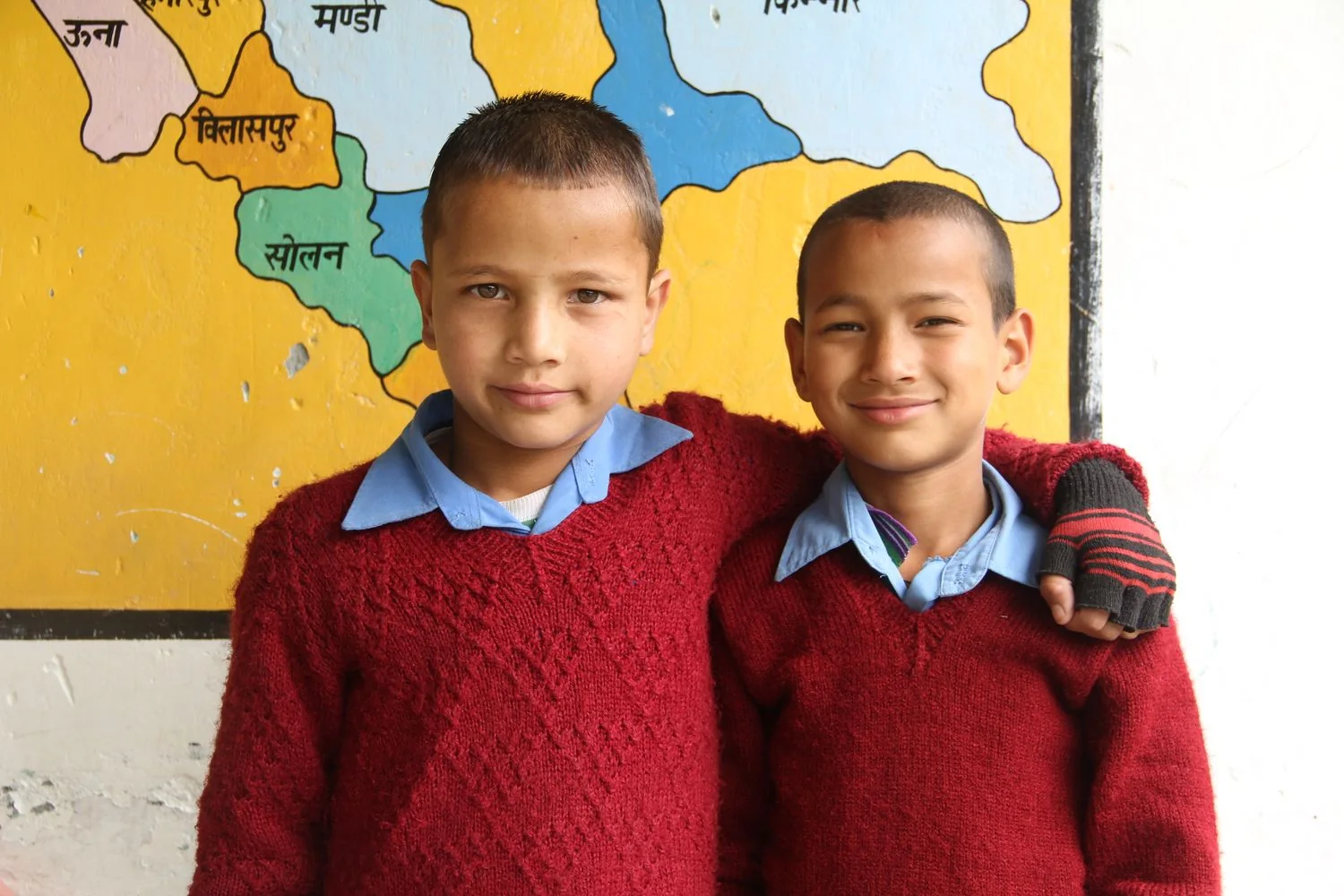 Two smiling schoolboys in red sweaters in a classroom